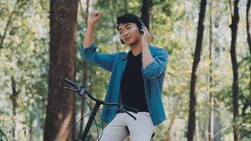 un hombre empuja un bicicleta y camina felizmente a relajarse en el parque después ciclismo para ejercicio. video