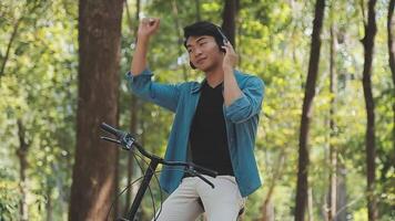 un hombre empuja un bicicleta y camina felizmente a relajarse en el parque después ciclismo para ejercicio. video