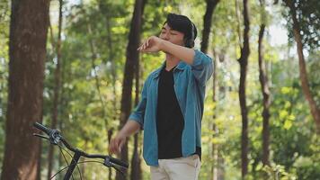 un hombre empuja un bicicleta y camina felizmente a relajarse en el parque después ciclismo para ejercicio. video