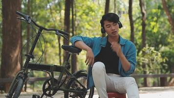 un hombre empuja un bicicleta y camina felizmente a relajarse en el parque después ciclismo para ejercicio. video