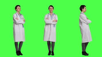 Portrait of successful physician standing with arms crossed against greenscreen backdrop, wearing a white coat and stethoscope. Doctor feeling confident with healthcare expertise. Camera A. video