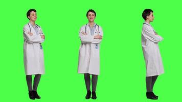 Portrait of successful physician standing with arms crossed against greenscreen backdrop, wearing a white coat and stethoscope. Doctor feeling confident with healthcare expertise. Camera A. video