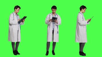 General practitioner studying radiography scan results for patients with disease, stands against greenscreen backdrop. Medic examines x ray diagnosis, works with a tablet. Camera A. video