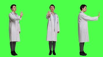 Woman physician raising palm and doing stop sign in studio, expressing rejection and denial against greenscreen backdrop. General practitioner showing warning symbol with negative reaction. Camera A. video