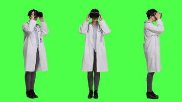 médico usa virtual realidade interativo lente em fone de ouvido dentro estúdio, Verificações diagnóstico com artificial inteligência três dimensional ferramenta. médico trabalho com vr óculos contra tela verde. Câmera uma. video