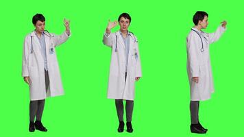 Friendly physician inviting people to come closer to her against greenscreen backdrop, calling patients over and smiling. General practitioner asking persons to approach her. Camera A. video