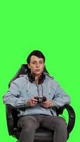 Front view Woman gamer playing online video games with controller, sitting in an office chair against greenscreen backdrop. Joyful person having fun with e sport competition, modern gaming setup. Camera B.