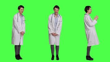 Portrait of general practitioner laughing at something against greenscreen backdrop, feeling joyful and confident with her healthcare expertise. Woman medic in white coat smiling in studio. Camera A. video