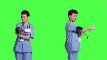 médico asistente demostración tonómetro usado a medida arterial sangre presión, en pie en contra pantalla verde fondo. enfermero trabajando con esfigmomanómetro herramienta a tomar medición a chequeo. cámara b. video