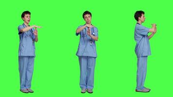 Medical assistant giving timeout symbol against greenscreen backdrop, showing limits and asking for a break. Nurse doing pause or stop gesture while she wears blue scrubs. Camera A. video