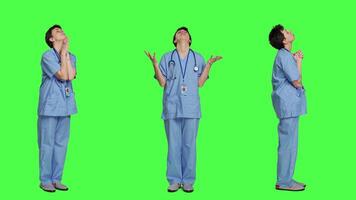 Hospital nurse worshipping God by prayer against greenscreen backdrop, praying to jesus christ and having hope in christianity and spirituality. Medical assistant doing meditation. Camera A. video