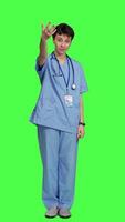 Front view Woman nurse waving hello and inviting people to come closer, calling over patients for checkup examinations against greenscreen. Medical assistant greeting persons and asking them to come. Camera A. video