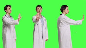 Woman physician raising palm and doing stop sign in studio, expressing rejection and denial against greenscreen backdrop. General practitioner showing warning symbol with negative reaction. Camera B. video