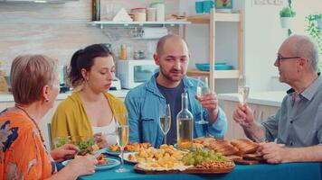 uomini fare clic e discutere durante il cena. Multi generazione, quattro le persone, Due contento coppie parlando e mangiare durante un' buongustaio pasto, godendo tempo a casa, nel il cucina seduta di il tavolo. video