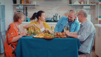 hombre utilizando teléfono durante cena demostración algunos imágenes a su madre. multi generación, cuatro gente, dos contento parejas hablando y comiendo durante un gastrónomo comida, disfrutando hora a hogar. video