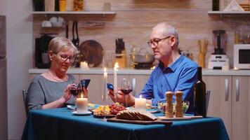 vecchio pensionato coppia utilizzando smartphone durante romantico cena. seduta a il tavolo nel il cucina, navigando, ricerca, utilizzando Telefono, Internet, festeggiare loro anniversario nel il cenare camera. video