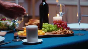 anziano pensionato uomo illuminazione il candela in attesa il suo moglie per romantico cena. anziano marito preparazione festivo pasto con sano cibo per anniversario celebrazione, seduta vicino il tavolo nel cucina. video