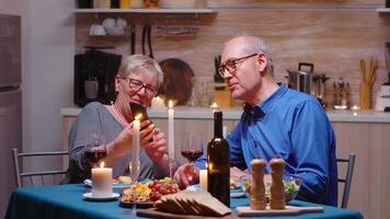Senior im Ruhestand alt Ehefrau zeigen Fotos auf Smartphone zu ihr Mann während romantisch Abendessen. Paar Sitzung beim das Tisch, reden, mit das Telefon, feiern ihr Jahrestag im das Essen Zimmer. video
