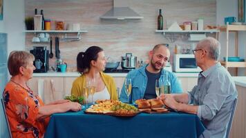 grootouders uitgeven een ontspannende familie dag. multi generatie, vier mensen, twee gelukkig paren pratend en aan het eten gedurende een fijnproever diner, genieten van tijd Bij huis. video