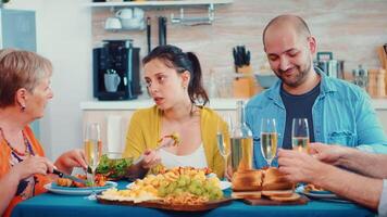 élargi famille interagir tandis que ayant une repas à à manger table dans le cuisine. multi génération, quatre personnes, deux content des couples parlant et en mangeant pendant une gourmet dîner, profiter temps à maison. video