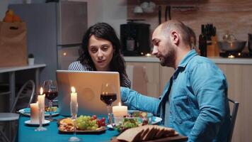 aufgeregt kaukasisch Liebhaber Paar Essen zusammen und mit Laptop. Erwachsene Sitzung beim das Tisch, suchen, durchsuchen, Surfen, mit Technologie, genießen das Mahlzeit im das Essen Zimmer video