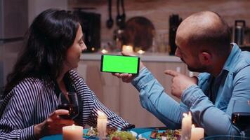 casado jovem casal segurando brincar telefone às jantar. feliz olhando às verde tela modelo croma chave isolado inteligente telefone exibição usando tecnologia Internet sentado às a mesa dentro cozinha. video