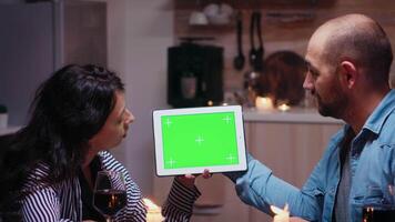 Jeune caucasien couple en utilisant vert maquette écran numérique isolé tablette ordinateur. mari et épouse à la recherche à vert écran modèle chrominance clé afficher séance à le table dans cuisine pendant dîner. video