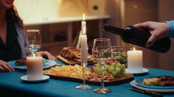 fechar acima do jovem homem derramando vermelho vinho dentro esposa vidro. romântico caucasiano feliz casal sentado às a mesa dentro cozinha a comemorar com vela luzes, amor e aniversário. romance surpresa dentro relação video