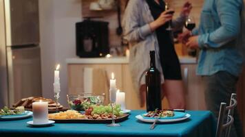 Young caucasian couple flirting during festive dinner with table in foreground. Adults having romantic date at home in the kitchen, drinking red wine, talking, smiling enjoying the meal in dining room video