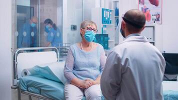 vecchio anziano donna avendo un' medico consultazione durante covid-19 pandemia, indossare un' maschera e medico nel protettivo indossare. moderno ospedale o privato clinica. assistenza sanitaria sistema video