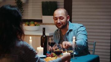 Pareja comiendo y Bebiendo vino con hombre en primer plano durante festivo cena en el cocina. hablando contento sentado a mesa comida habitación, disfrutando el comida a hogar teniendo romántico hora a vela luces video