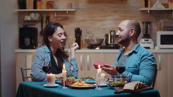 Jeune caucasien homme surprenant femme avec cadeau pendant de fête dîner séance à le table dans le cuisine. content de bonne humeur couple à manger ensemble à maison, profiter le repas célébrer leur anniversaire video