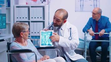 Doctor showing brain X ray image to elderly senior woman in a wheelchair, in a recovery clinic or hospital. Modern health care treatment, rehabilitation program for invalids and handicapped persons video
