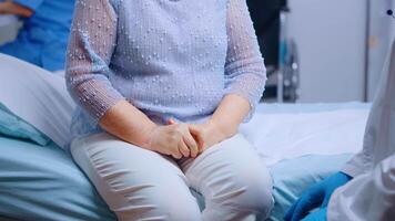 Close up of doctor hands in blue protective gloves comfortin a stressed old woman sitting on hospital bed in modern private clinic. Global pandemic coronavirus covid-19 healthcare pandemic video