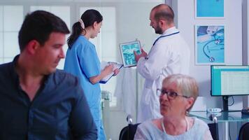 Doctor pointing at tablet pc with patient x-ray while discussing with nurse in hospital hallway. Doctor wearing white coat and stethoscope. Health care system medical diagnosis disease teamwork video