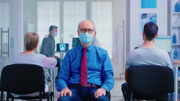 retrato de mayor hombre con cara máscara en contra coronavirus en hospital esperando zona mirando a cámara. pacientes durante codicioso brote en clínica esperando para examen. video