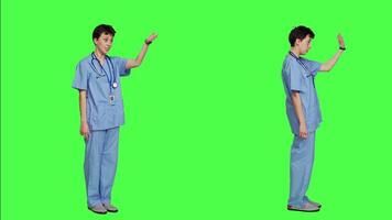 Medical assistant calling people over to come closer for examination, inviting patients at cabinet for checkup. Nurse with scrubs stands against greenscreen, come at me concept. Camera A. video