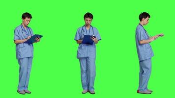 Confident hospital nurse taking notes for the next medic appointment, standing over greenscreen backdrop. Medical assistant with uniform writing patient information on clipboard papers. Camera A. video