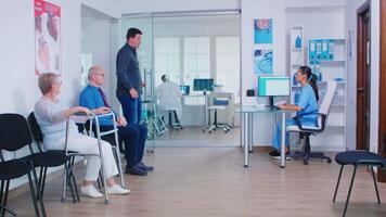 Nurse giving direction to patients at hospital reception. Disabled woman with walking frame in clinic waiting area. Assistant inviting patient in consultation office. video