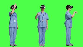 Health specialist using vr headset to examine patient diagnosis, stands against greenscreen backdrop. Nurse works with artificial intelligence virtual reality glasses, three dimensional. Camera A. video