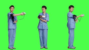 Medical assistant showing tonometer used to measure arterial blood pressure, standing against greenscreen backdrop. Nurse working with sphygmomanometer tool to take measurement at checkup. Camera A. video