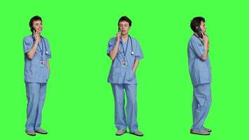 Health specialist using smartphone to make important calls, standing against greenscreen backdrop. Nurse talking to patients for checkup exams on telephone line, calling people to confirm. Camera A. video