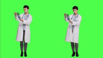 Woman doctor examines x ray scan to find disease diagnosis for patient, looking at radiography results to determine illness and cure. Medic standing against greenscreen backdrop. Camera A. video