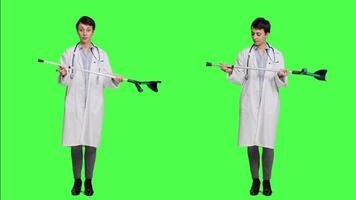 Woman physician showing crutches use to help with mobility in case of bone fracture, rehabilitation and recovery after an injury. Medic holds orthopedics tool against greenscreen. Camera A. video