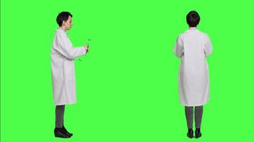 mujer médico es utilizando un estetoscopio a escucha a respiración en estudio, vistiendo un blanco hospital Saco en contra pantalla verde fondo. médico con profesional pericia lo hace consultas cámara una. video