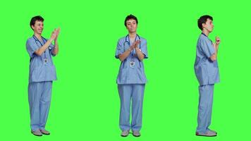 Smiling medical assistant applauding someone in studio, celebrating success and cheering against greenscreen backdrop. Young nurse clapping hands and feeling happy about achievement. Camera A. video