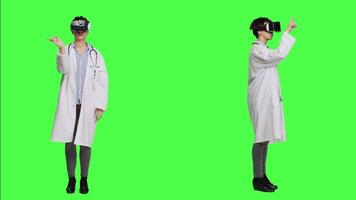 Physician consulting patients with virtual reality futuristic glasses, wears white coat against greenscreen backdrop. General practitioner uses artificial intelligence interactive headset. Camera A. video