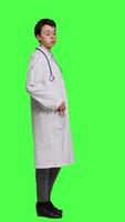 Profile Woman physician looking around for patients to come at checkup exams, waiting for someone standing against greenscreen backdrop. General practitioner with white coat feeling impatient. Camera A. video