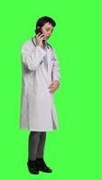 Side view Woman doctor talking on smartphone call against greenscreen backdrop, answering phone line to make an exam appointment for a patient. Physician uses mobile phone to chat with people. Camera A. video