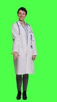 Front view Woman medic does web advertisement against greenscreen backdrop, pointing to left and right sides in studio. Doctor with white coat advertising something for a commercial. Camera A. video